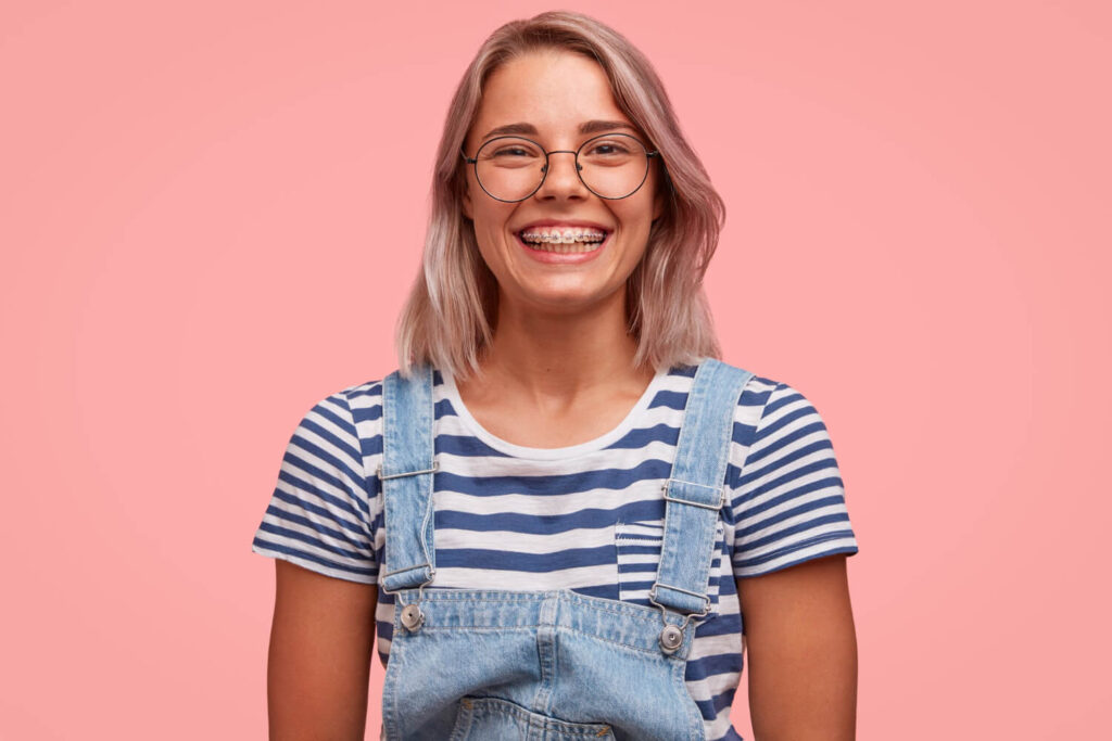 Jovem de óculos sorrindo com aparelho fixo metálico na Aliança Odontologia Itabaiana. Ideal para quem deseja trocar para alinhadores invisíveis.