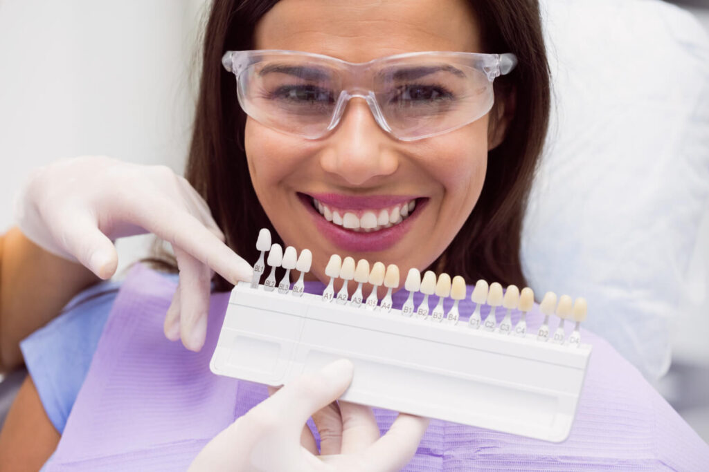 Dentista selecionando escala de cores para facetas de resina em paciente sorridente na Aliança Itabaiana.